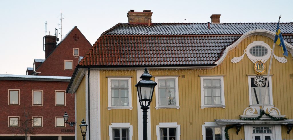 Bild på Ulricehamns rådhus, en gul träbyggnad som är stadens äldsta byggnad. I bakgrunden stadshuset i rött tegel.