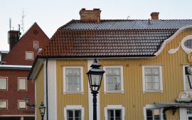 Bild på Ulricehamns rådhus, en gul träbyggnad som är stadens äldsta byggnad. I bakgrunden stadshuset i rött tegel.