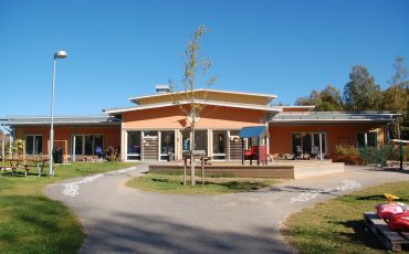 Bild på Stadsskogens förskola en solig dag. Gården i förgrunden och förskolan i bakgrunden.