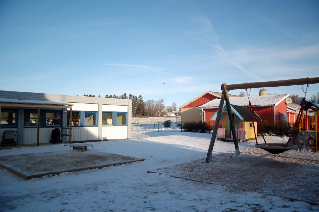 Bild på Träskons förskola med ett snötäcke på lekplatsen. Huset är en låg mindre byggnad med platt tak.