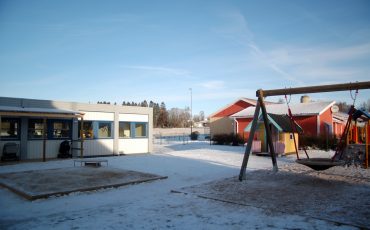 Bild på Träskons förskola med ett snötäcke på lekplatsen. Huset är en låg mindre byggnad med platt tak.