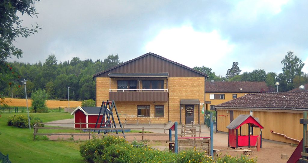 Bild på junibackens förskola med lekplatsen i förgrunden. huset är av gult tegel och brunt trä och är i två våningar