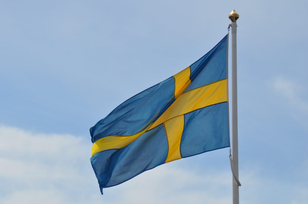 Svenska flaggan. Blå med ett gult kors, vajar på en flaggstång