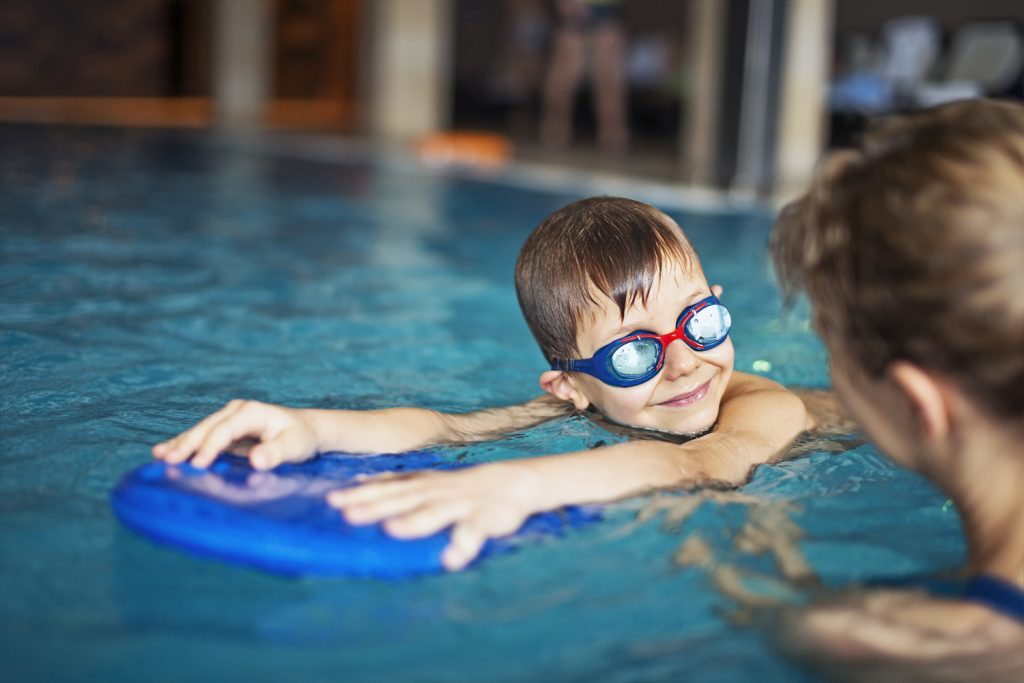 Bild på barn som simmar med en flytdyna och har simglasögon.