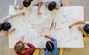 Bild på barn som ritar en skola på ett papper lika stort som ett bord.