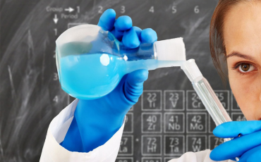 Bild på elev med blå handskar som häller blå vätska i en behållare