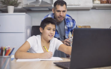 Bild på en pappa som hjälper sin son med läxorna vid datorn