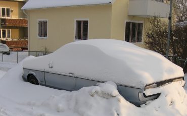Bild på bil parkerad framför hus, gömd i snö.