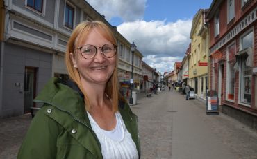 Bild på medelålders kvinna i grön jacka som leende står med gågatan i Ulricehamn i bakgrunden. Linda Larsson Järleklint på gågatan i Ulricehamn.