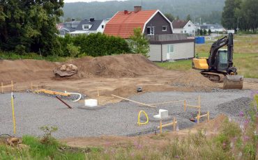 Bild på en tomt som håller på att markberedas av en grävskopa. ett färdigbyggt hus i bakgrunden.