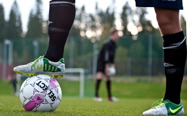 En bild på en fotbollsspelares ben som håller fast en fotboll med foten.