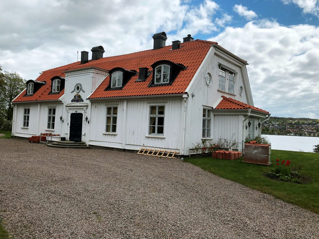 Bild på huvudbyggnaden på Brunnsnäs herrgård. En vit byggnad med tegeltak och sjön i bakgrunden.