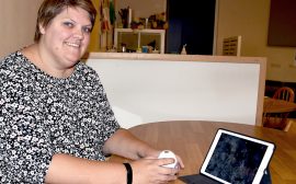 Bild på Ida Hoffren, en korthårig kvinna som sitter vid ett bord med den ipad och ler in i kameran.