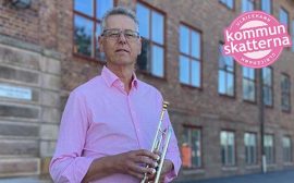 Man med trumpet framför tegelbyggnad.