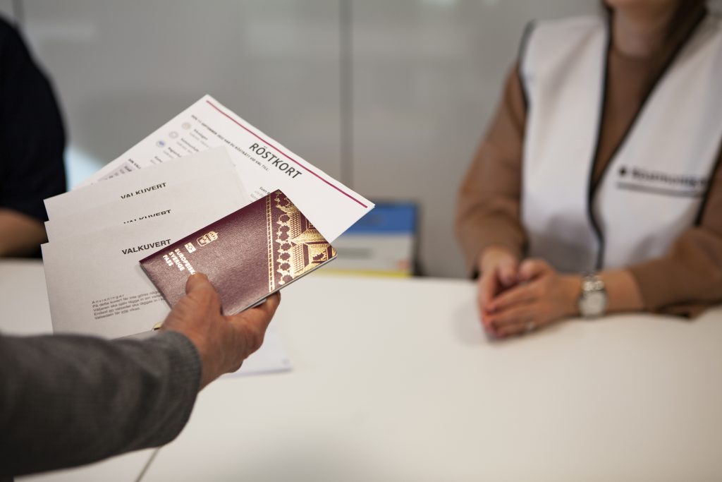 En bild på en hand som håller i ett valkuvert och ett pass.