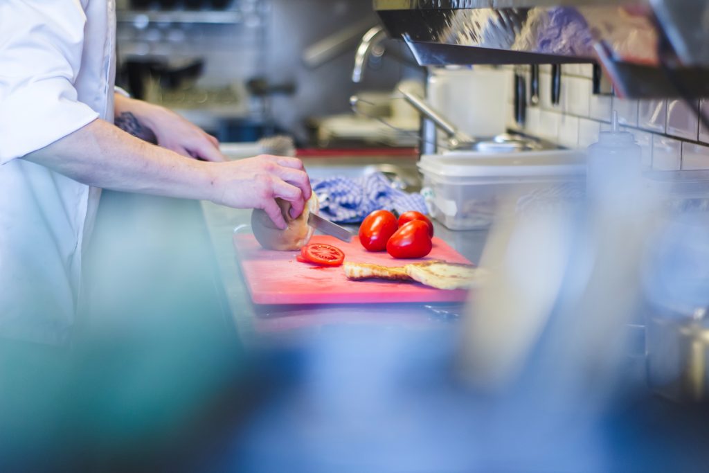 Kock som skär tomater i ett kök