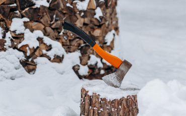 Yxa i stubbe framför staplade vedträn