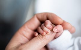 En stor hand håller i en nyfödd bebis hand.