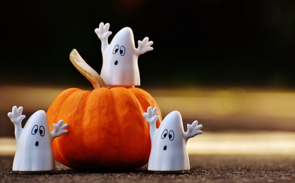 Tre vita spöken står runt en orange pumpa