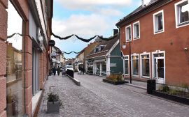 Vy över gågatan. Färgglada hus, gatsten, planteringskärl, räcken och belysningsstolpar syns.