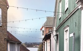 Linspänd belysning mellan brandgult tegelhus och grönt trähus med vita knutar.