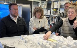 Tre personer tittar på modell föreställande en del av en stad