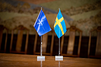Två flaggor på ett bord, den ena med nato-emblemet, den andra med svenska flaggan.