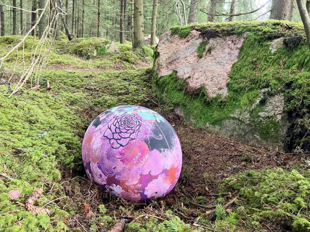 Stort lilamålat ägg ligger i skogen vid en stor sten.