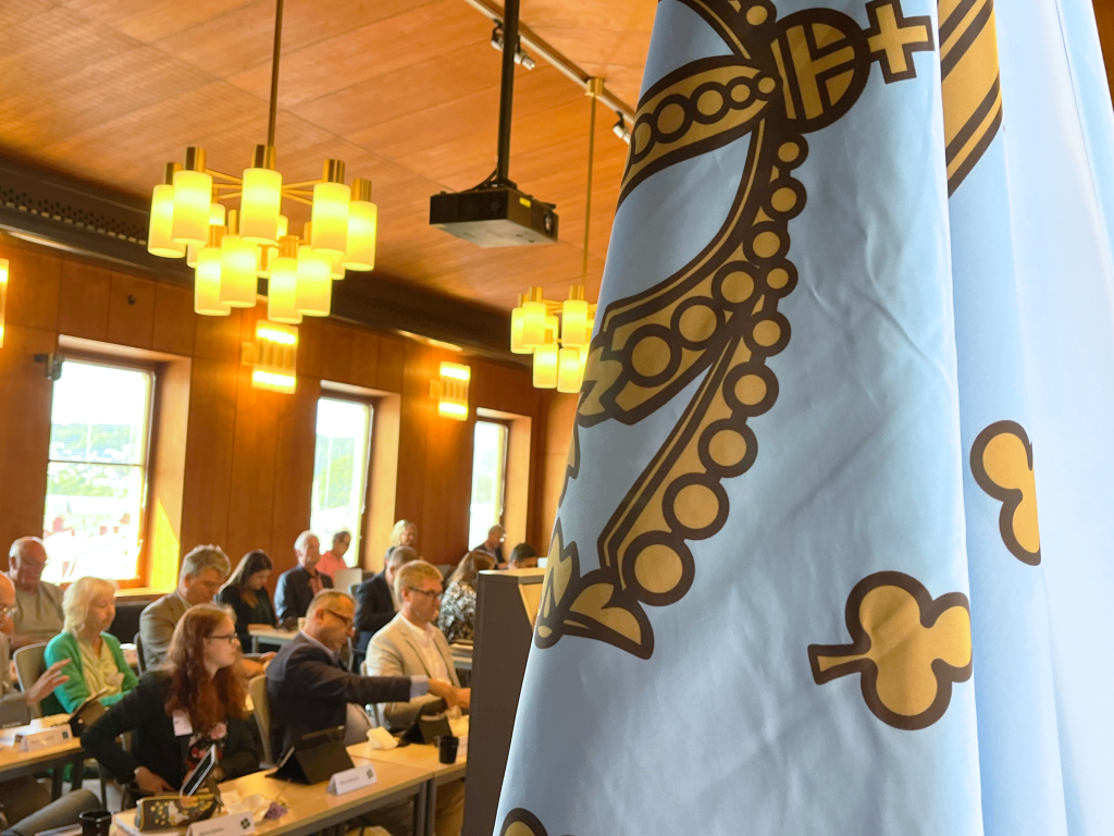 flera människor i en sal, bakom en flagga