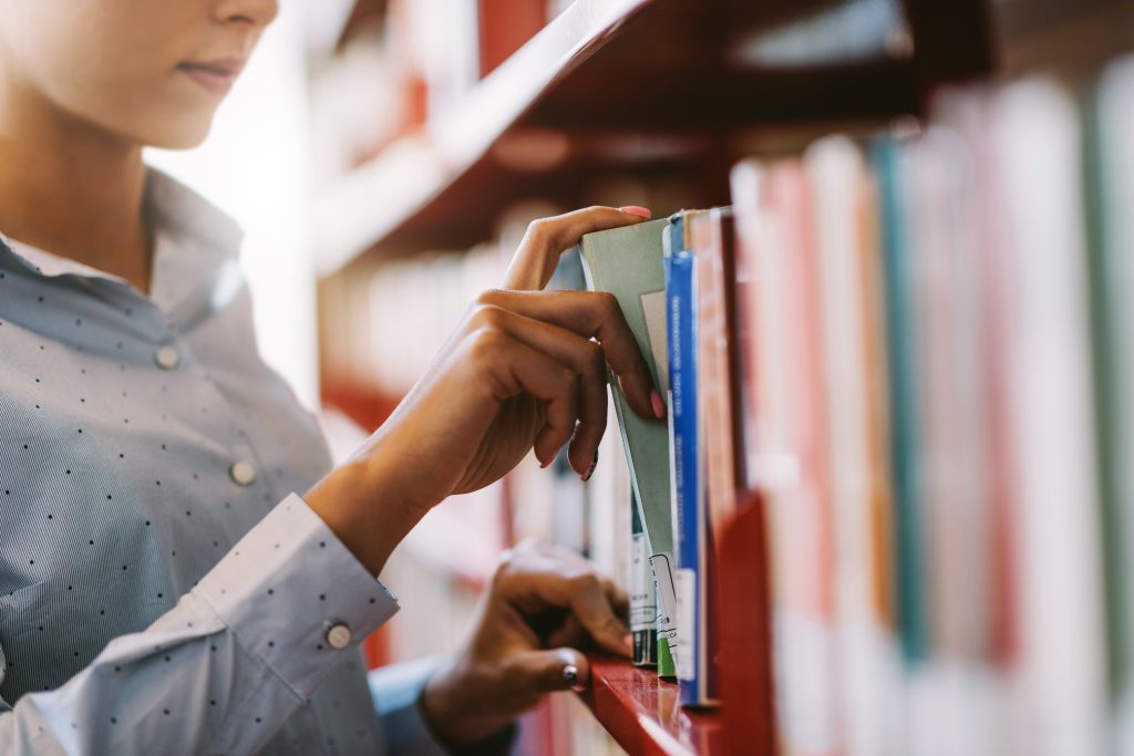 Person tar ut en bok från en bibliotekshylla med böcker