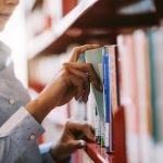 Person tar ut en bok från en bibliotekshylla med böcker